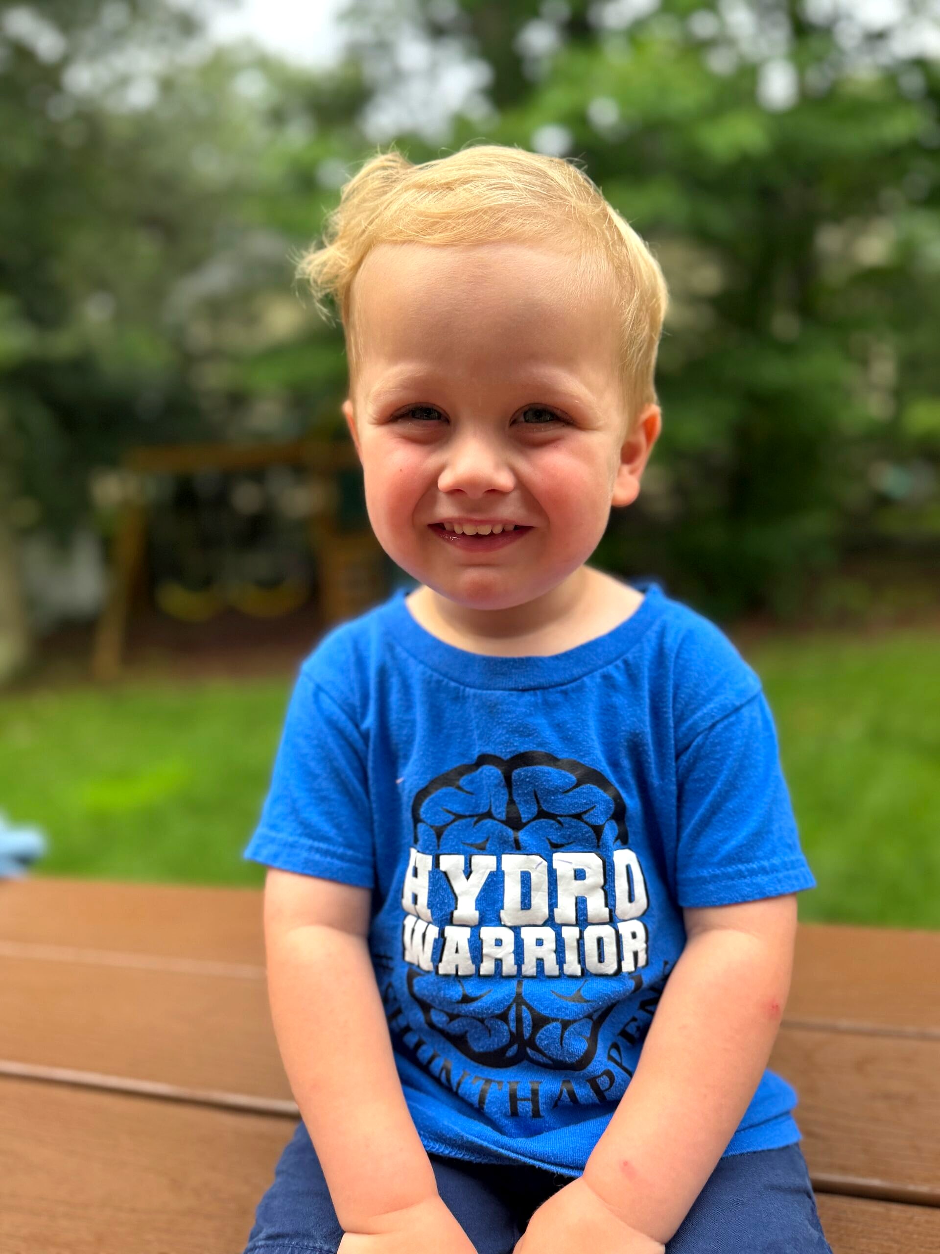 A smiling toddler in a blue Hydro Warrior t-shirt